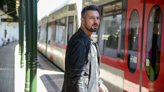 Murathan Muslu in schwarzer Lederjacke steht am Bahnsteig vor einem Zug.