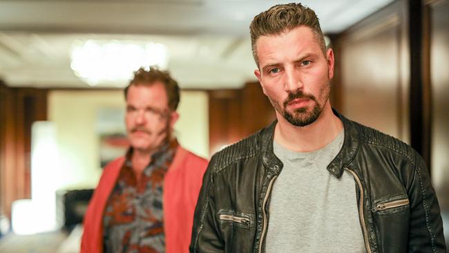 © ORF/Petro Domenigg Valentin "Itchiy" Janusovic steht in einem beleuchteten Raum und blickt nach vorne, im Hintergrund steht Berischer.