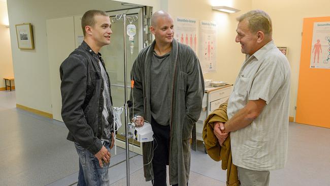 © ORF/Hubert Mican In einem Klinikflur stehen Sylvester Thaler und Wilmer Eberts bei Florian Fehenberger, der an einem Infusionsständer hängt.