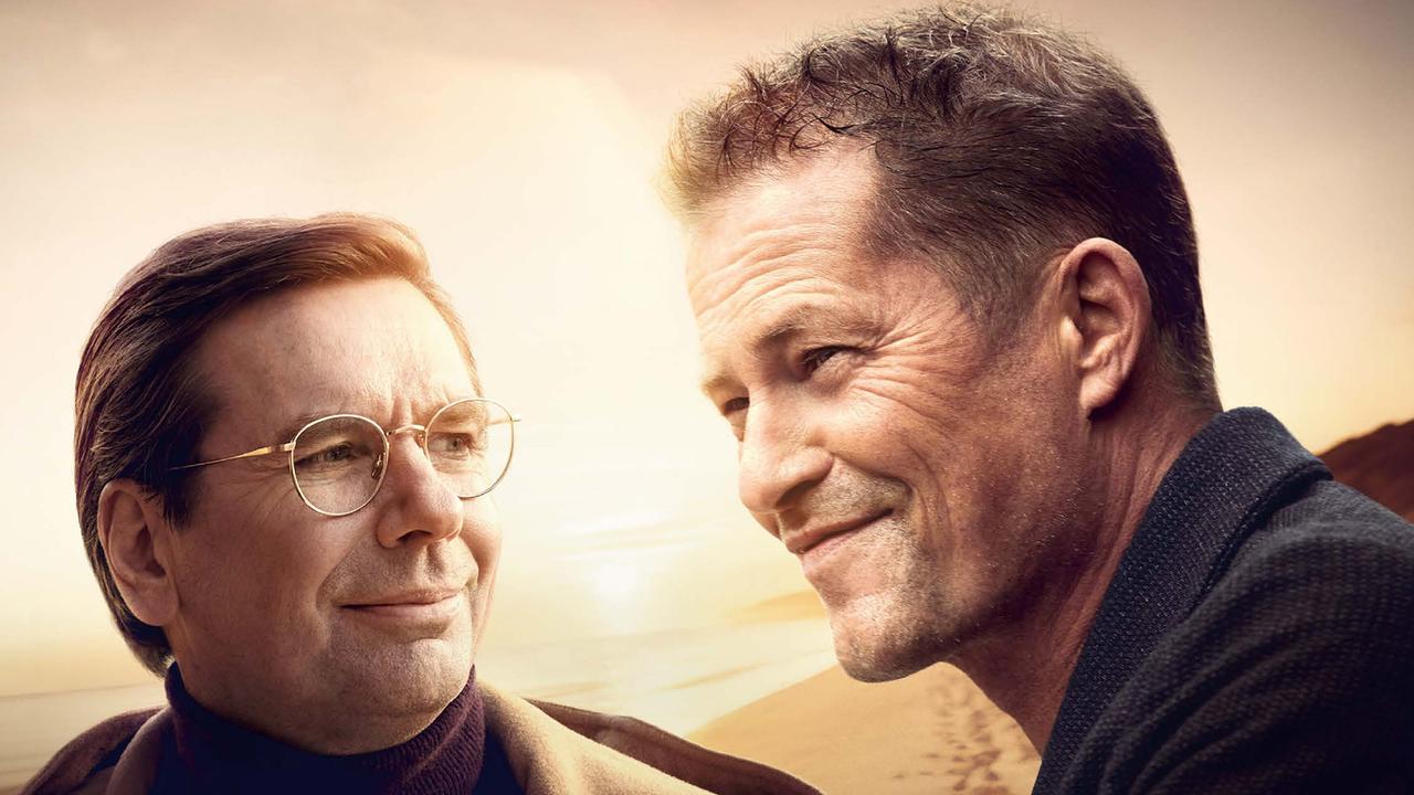 Michael Maertens als Arthur mit Brille und Til Schweiger als Felix stehen nebeneinander, beide lächeln freundlich und blicken aneinander vorbei