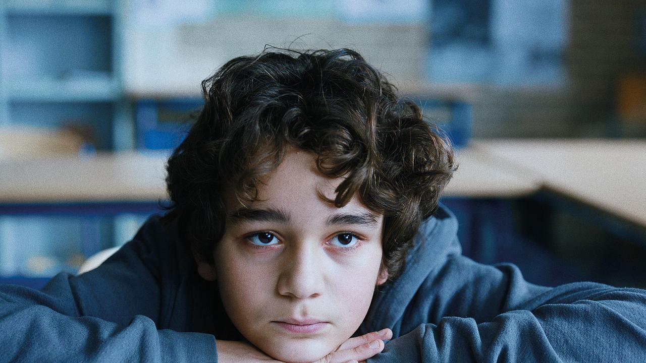 Leonard Stettnisch als Schüler Oskar - im Klassenzimmer sitzt er an seinem Tisch, mit dem Kinn auf seinen auf der Tischplatte gefalteten Händen blickt er vor sich hin