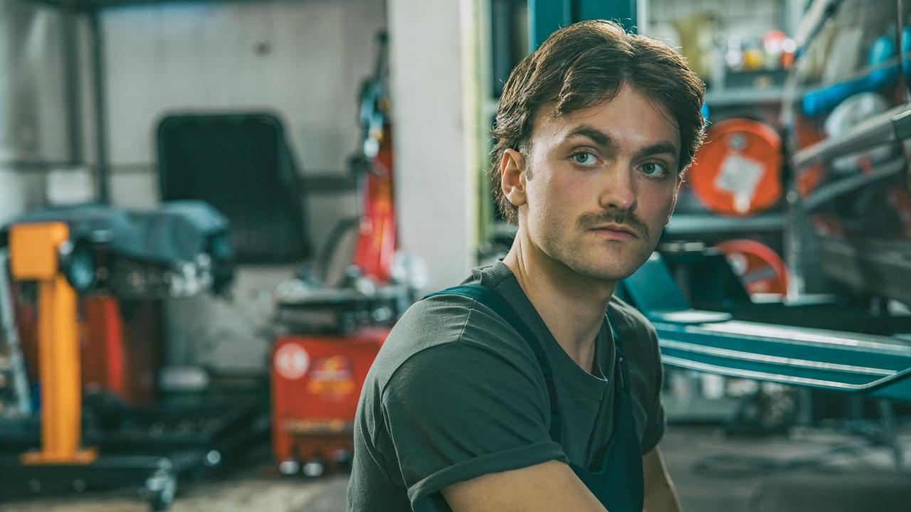© ORF/ARD Degeto/Mona Film/Victoria Herbig In der Werkstatt von Broszeks Autohandel: Mechaniker Roman repariert gerade ein Auto. Er hört Jonas und Broszek bei ihrem Gespräch zu.