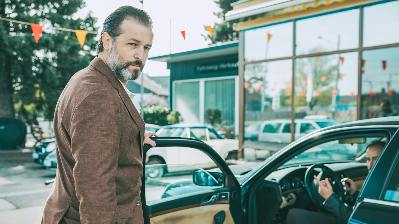 © ORF/ARD Degeto/Mona Film/Victoria Herbig Autohaus Broszek: Andreas Broszek steht an der geöffneten Tür des Autos von Michael Axmann, der gerade eingestiegen ist.