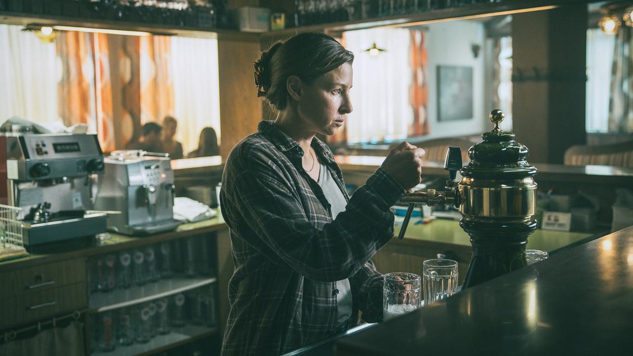 © ORF/ARD Degeto/Mona Film/Victoria Herbig Caro, die Mutter des Opfers, zapft Bier hinter einer Bar im Gasthaus für ihre Gäste.