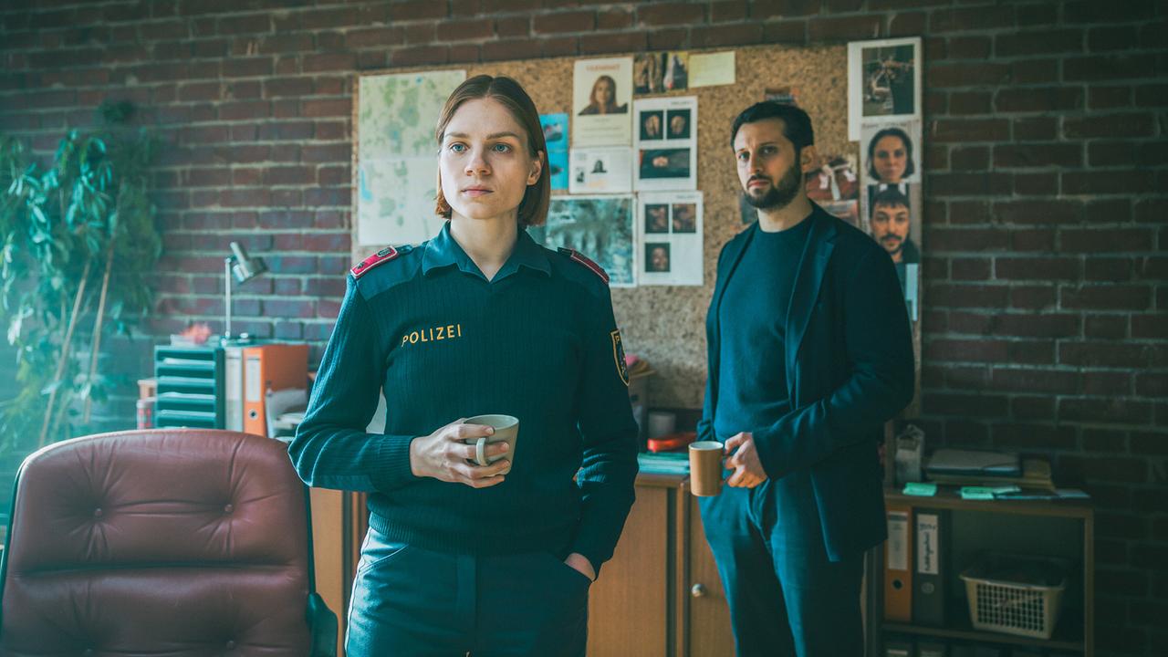 © ORF/ARD Degeto/Mona Film/Victoria Herbig Polizeidienststelle in Pias Büro: Polizistin Elli und Tarek Moser stehen vor der Pinwand und sehen zu wie der Laptop übergeben wird.