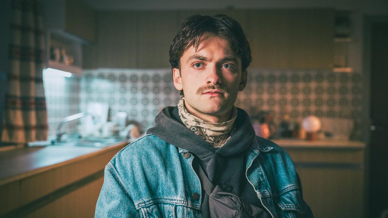Roman sitzt in seiner Küche am Küchentisch und wird von Broszek bedroht.