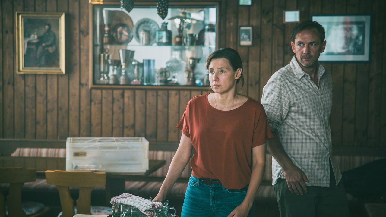 Im Gasthaus bei der DNA-Reihentestung: Caro, die gerade Getränkegläser abgestellt hat und Gerry sehen zur Eingangstür, als Roman und Broszek hereinkommen.