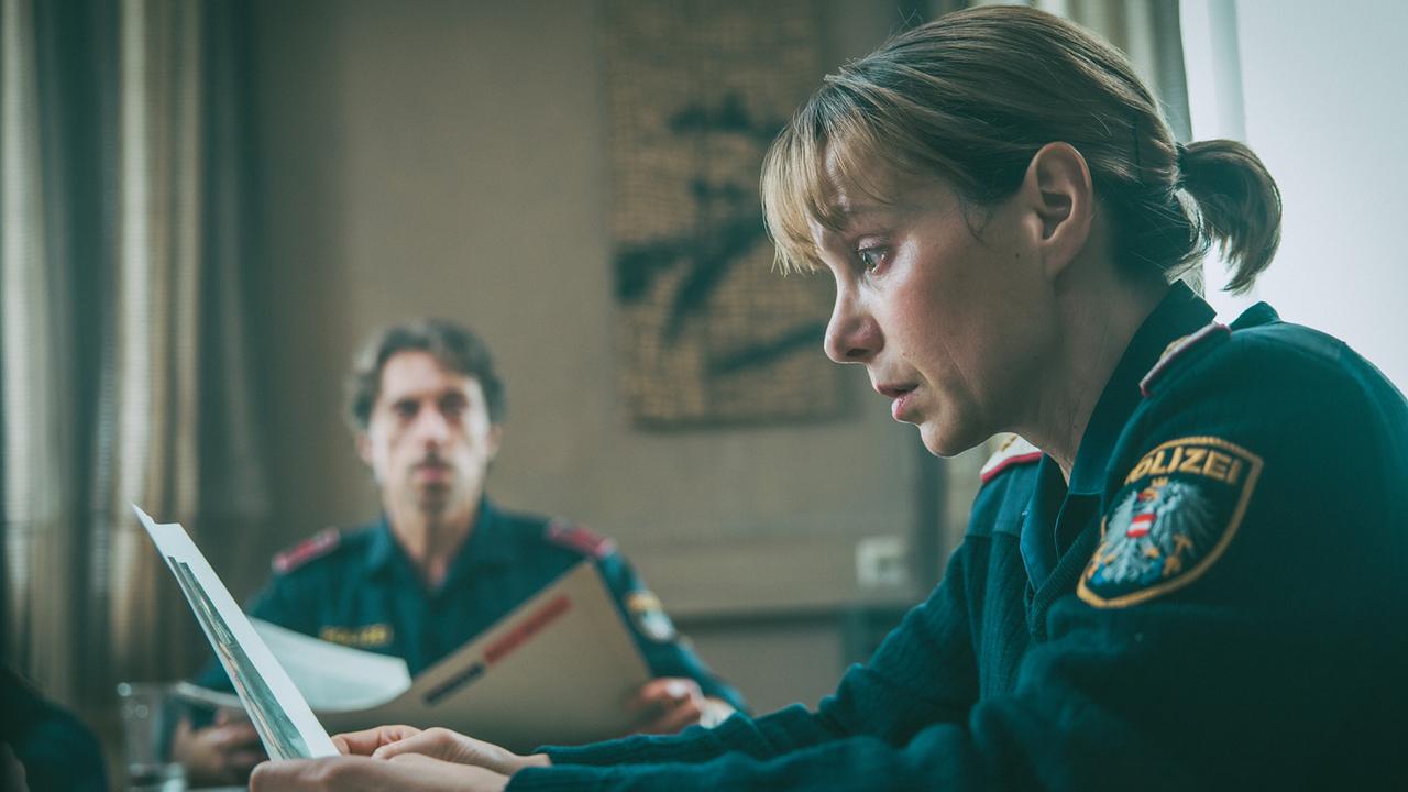  In der Polizeidienststelle nach der Sichtung eines Videos von Amelie: Lukas blickt zu Pia, die eines von Amelies freizügigen Fotos in der Hand hält.