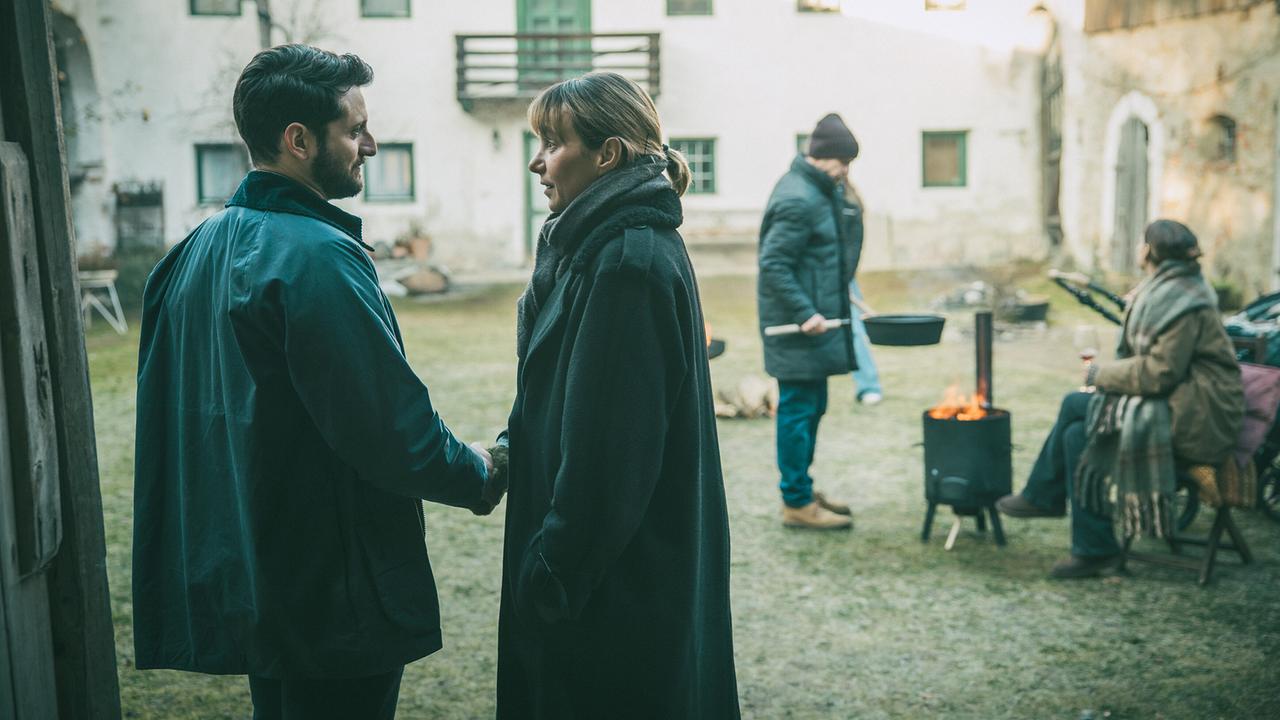 Bei Pias Geburtstagsfeier im Hof der Familie Kraus: Die demente Pia stellt sich ihrem "alten/neuen" Freund Tarek vor. Im Hintergrund steht ihr Mann Jonas neben ihre Schwester Caro an einer Feuerstelle.