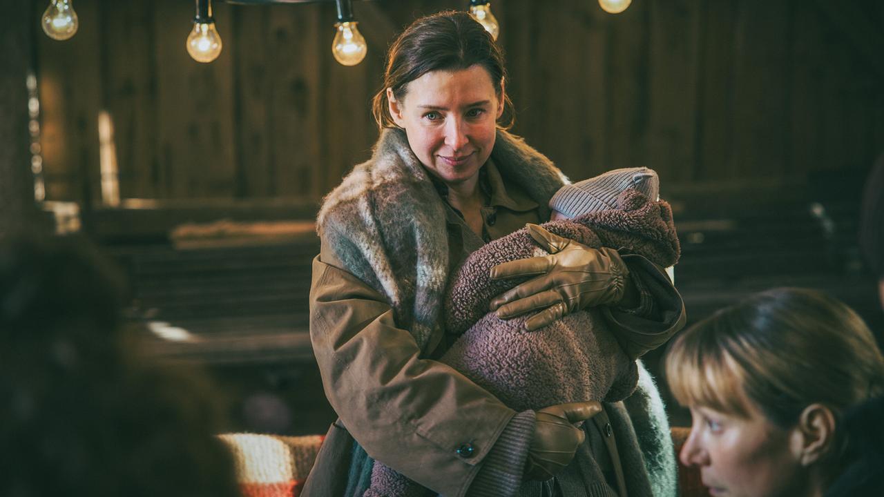 Caro steht mit Baby Milo im Arm bei der Geburtstagsfeier ihrer Schwester Pia in der Scheune der Familie Kraus.