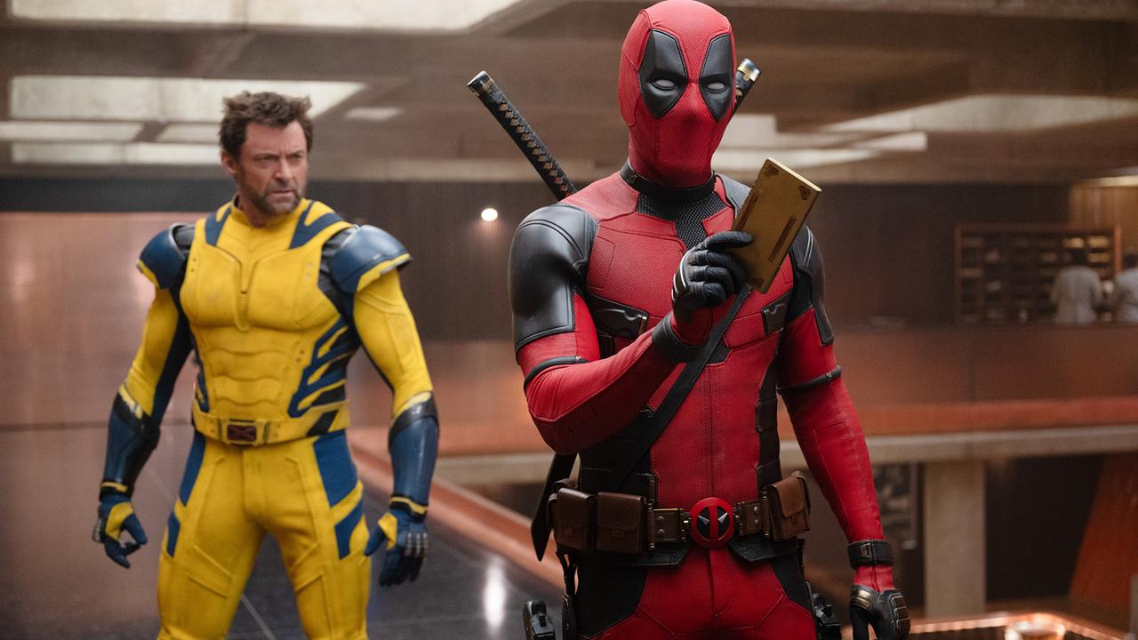 © ORF/Disney/20th Century Studios/Marvel/Jay Maidment Hugh Jackman als Wolverine in einem gelb-blauen Anzug und Ryan Reynolds als Deadpool in rot-schwarzem Anzug stehen in einem Raum, Deadpool hält etwas in der Hand, das er seinem Gegenüber zeigt
