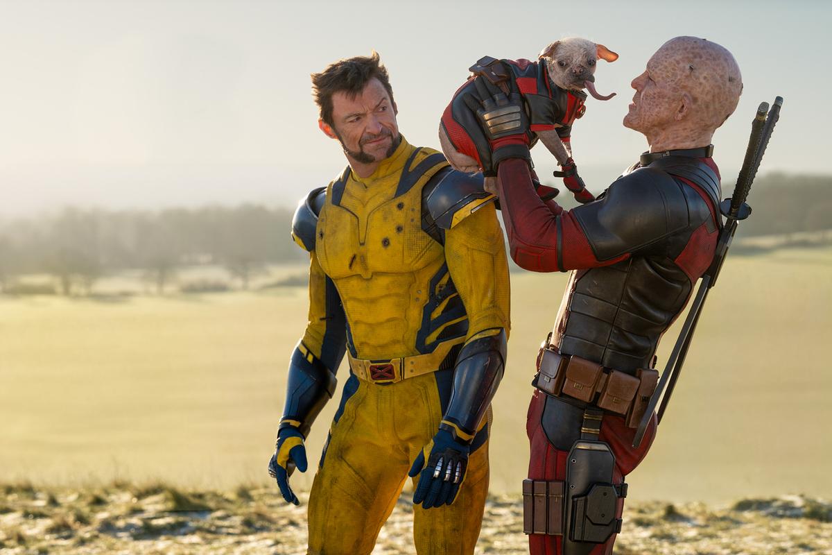 © ORF/Disney/20th Century Studios/Marvel/Jay Maidment Hugh Jackman als Wolverine in gelb-blauem Anzug und Ryan Reynolds als Deadpool rot-schwarzem Anzug, Deadpool hält einen Hund in die Luft, Wolverine blickt lächelnd zu ihm zurück