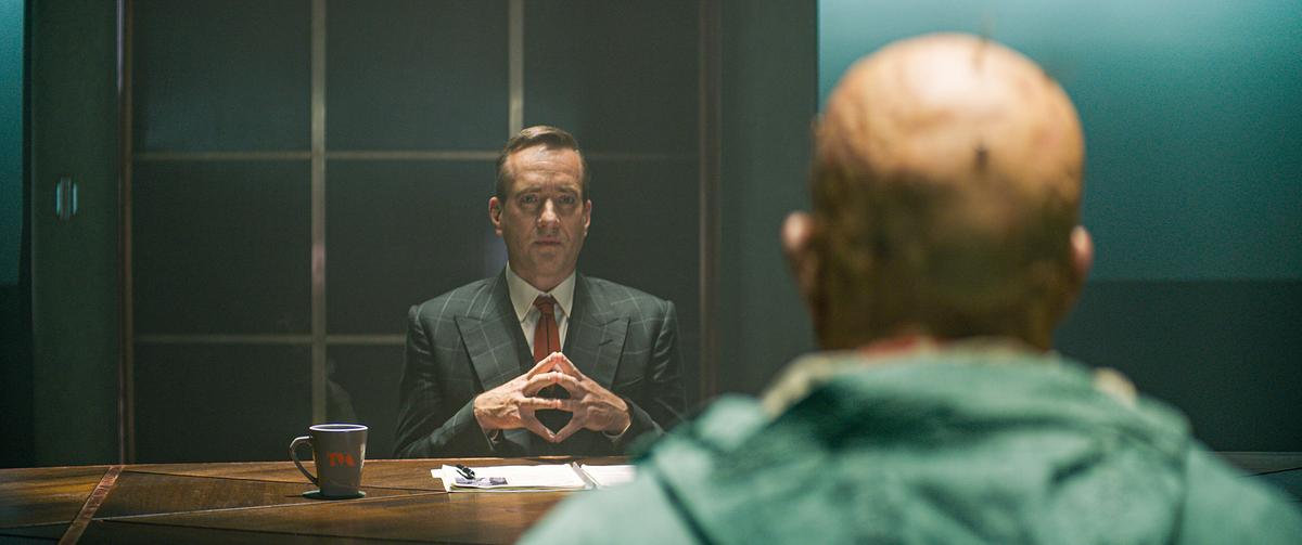 © ORF/Disney/20th Century Studios/Marvel Matthew Macfadyen sitzt als Mr. Paradox in einem Business-Anzug mit Krawatte an einem Schreibtisch, ihm gegenüber Ryan Reynolds als Wade Wilson