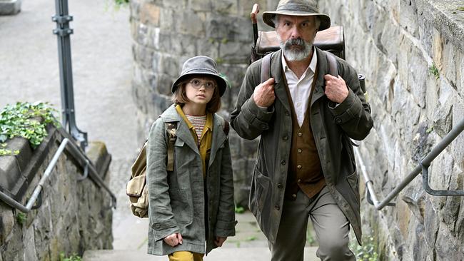 Christoph Maria Herbst als Buchspazierer Carl Kolhoff mit ledernem Rucksack steigt er in Begleitung von Yuna Bennett als Schascha eine steinerne Treppe hinauf