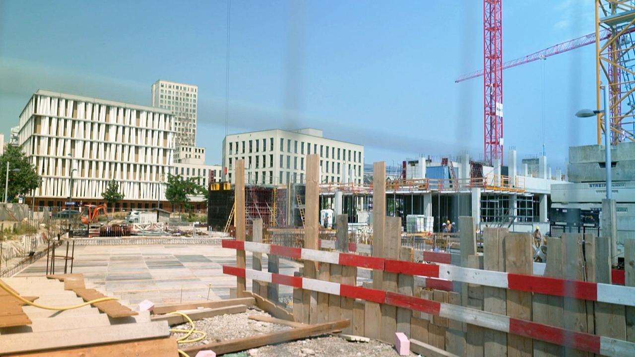 Baustelle in Wien, zwischen bereits errichteten Wohnhäusern ist die erste Etage eines Wohnhauses errichtet, umgeben von Kränen und Bauzäunen