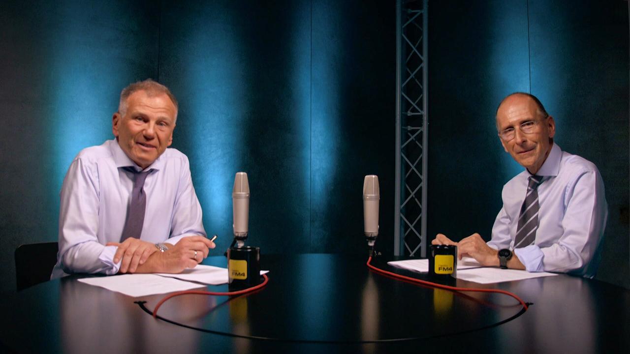 Armin Wolf und Peter Filzmaier mit Hemd und Krawatte sitzen an einem dunklen Tisch in einem Studio, vor ihnen jeweils ein Mikro und ein FM4-Häferl.