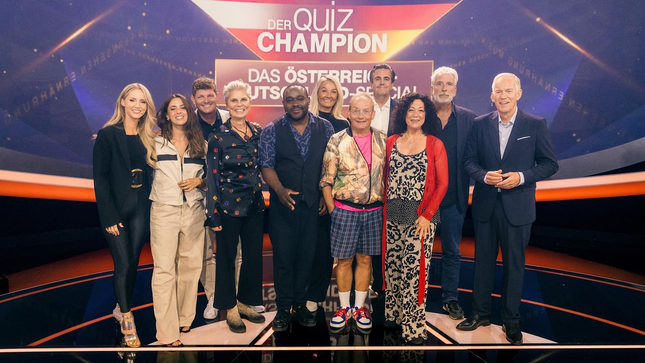 © ORF/ZDF/Thomas Kierok Melissa Naschenweng, Vanessa Mai, Thomas Morgenstern, Sarah Wiener, Nelson Müller, Franziska van Almsick, Wigald Boning, Bastian Pastewka, Barbara Wussow, Dirk Stermann und Johannes B. Kerner posieren im Studio vor der Grafik "Der Quiz Champion - Das Österreich-Deutschland-Special"