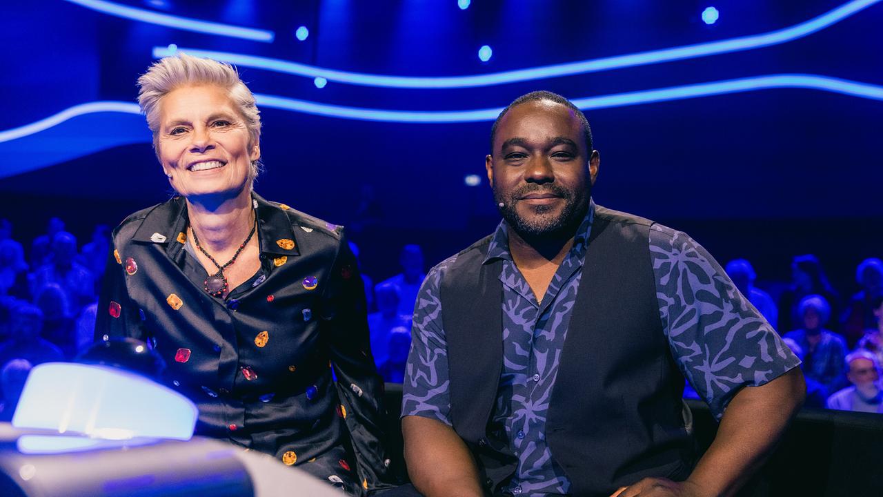 © ORF/ZDF/Thomas Kierok Sarah Wiener und Nelson Müller sitzen am blau beleuchteten Ratetisch der Kategorie „Ernährung“ vor dem Studiopublikum bei "Der Quiz Champion".