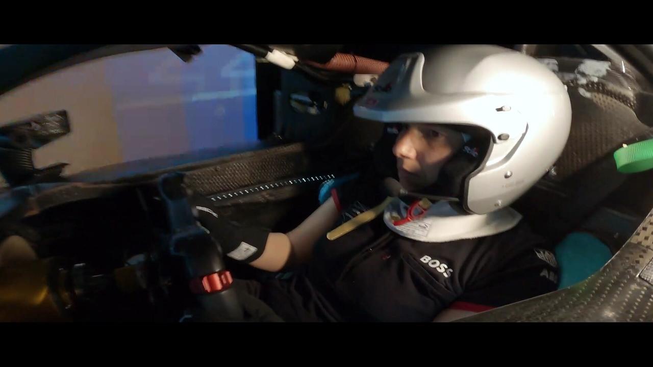 Motorsportlerin Simona de Silvestro im Rennanzug und mit Helm sitzt angeschnallt im Cockpit eines Rennwagens und hält das Lenkrad fest.