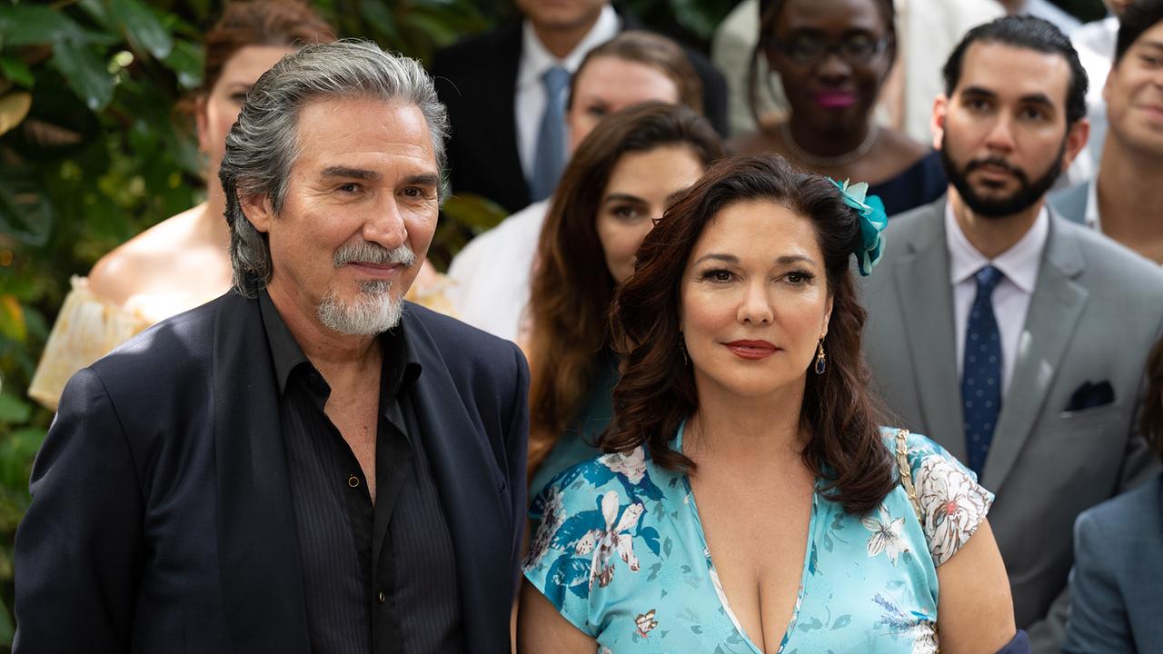 Die Eltern des Bräutigams, Pedro Damián als Hernan in schwarzem offenen Hemd unter dunklem Sakko und Laura Harring als Marcela Castillo in hellblaum, floral gemusterten Kleid