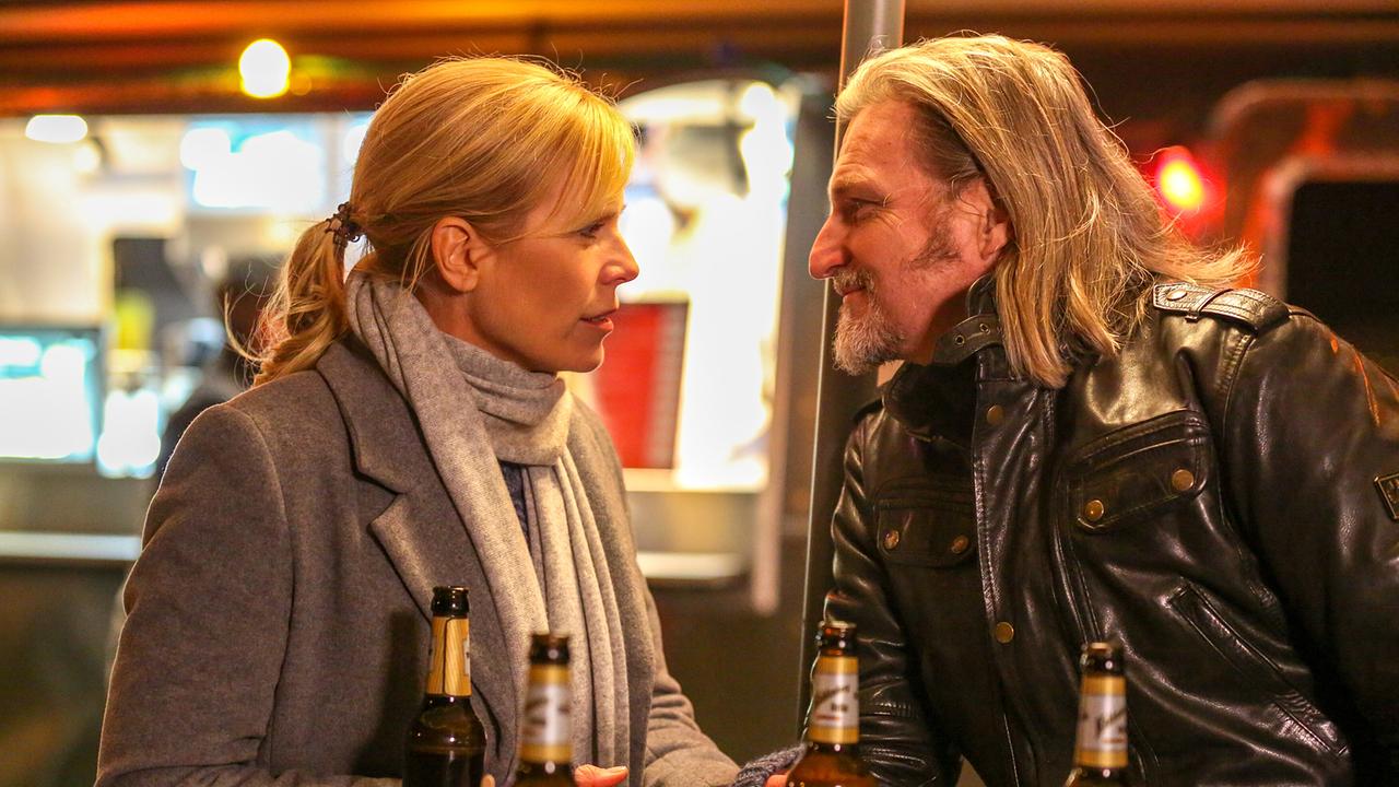 Ina Zimmermann und Carl Ribarski unterhalten sich nachts an einem Stehtisch, auf dem mehrere Bierflaschen stehen, vor einem Foodtruck.