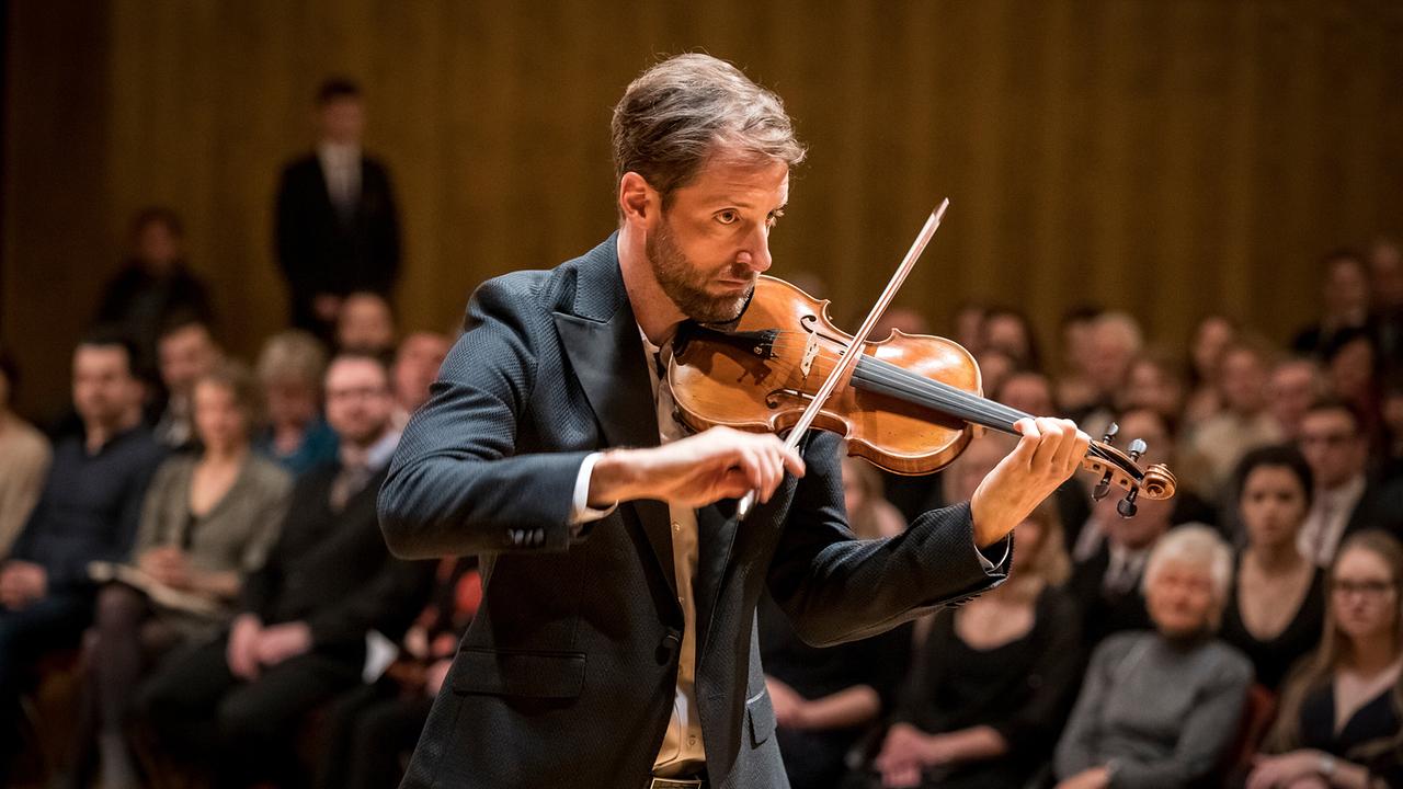 Der Geiger Philipp Baumgarten spielt in einem Konzertsaal vor sitzendem Publikum.
