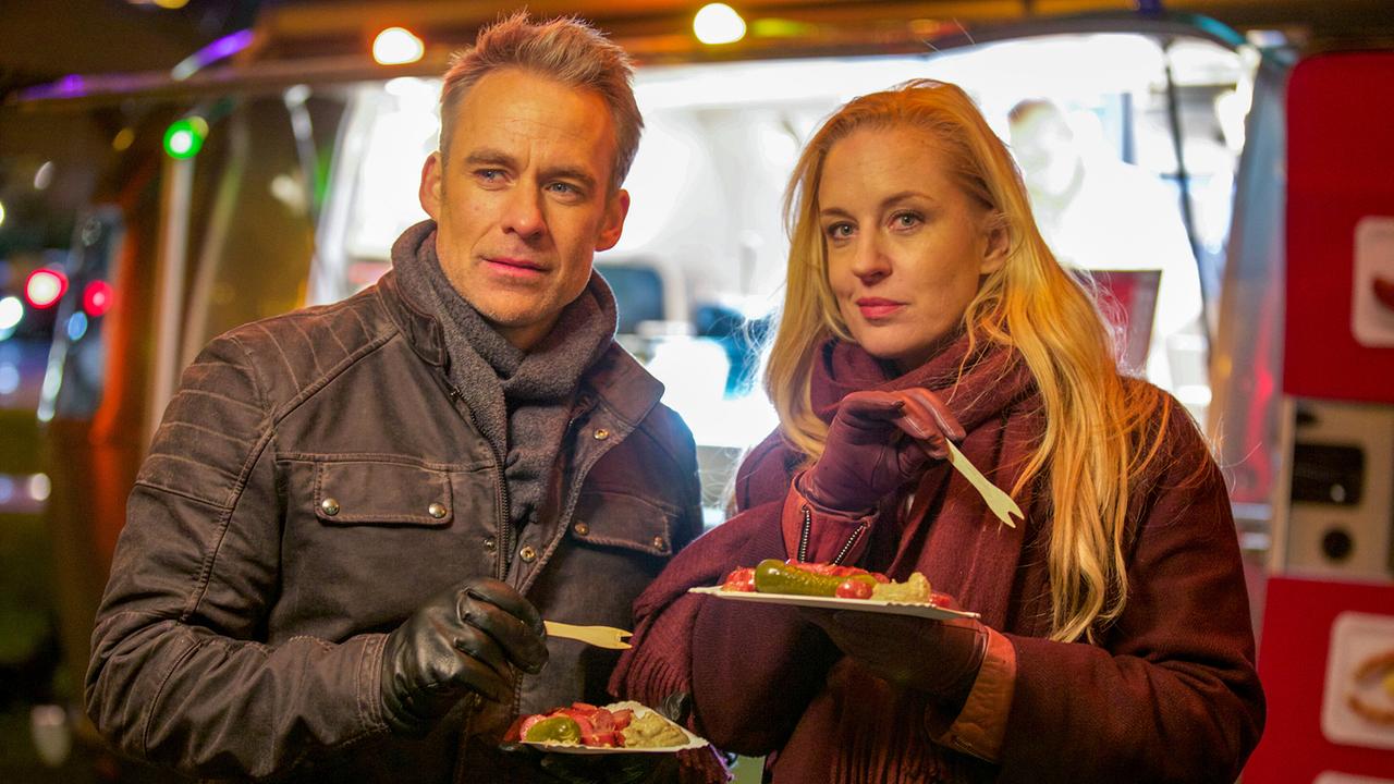 Jan Maybach und Penny Lanz stehen nebenander vor einem Foodtruck und essen Würsteln von Papptellern.