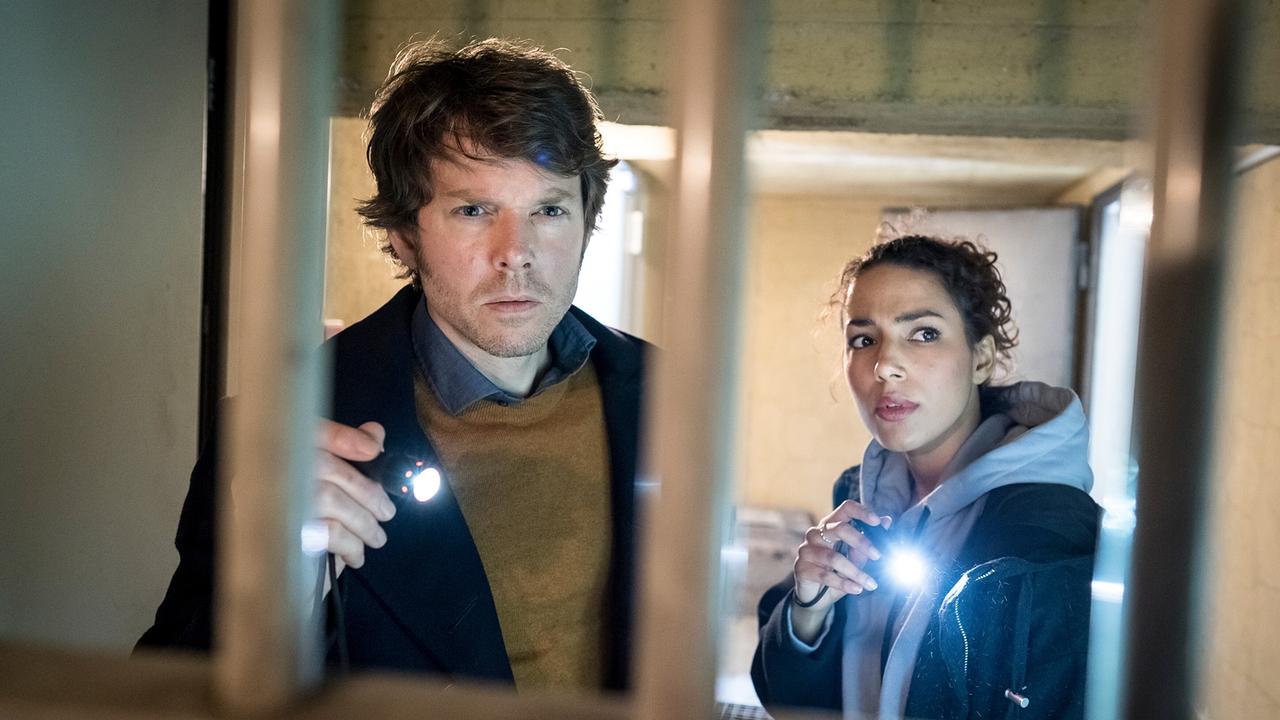 Tom Kowalski und Kim Nowak leuchten mit Taschenlampen durch ein Gitter in einen dunklen Raum.