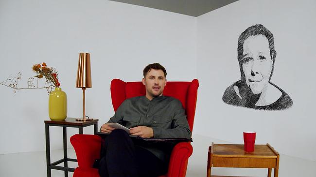 Moderator Ferdinand Seebacher sitz auf einem roten Stuhl, neben ihm stehen kleine Beistelltische, hinter ugm 