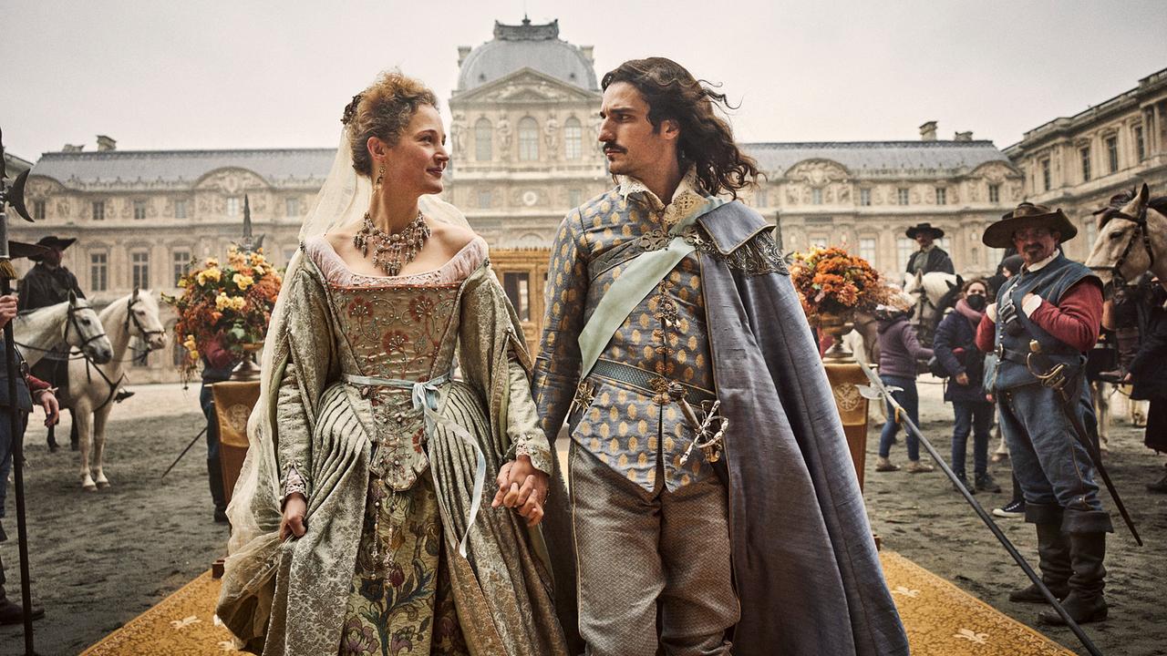 © ORF/Constantin Film/Ben King Eine Frau in einem prunkvollen Kleid und ein Mann in aufwendiger Mantel-und-Degen-Uniform gehen Hand in Hand vor einem prächtigen Palast