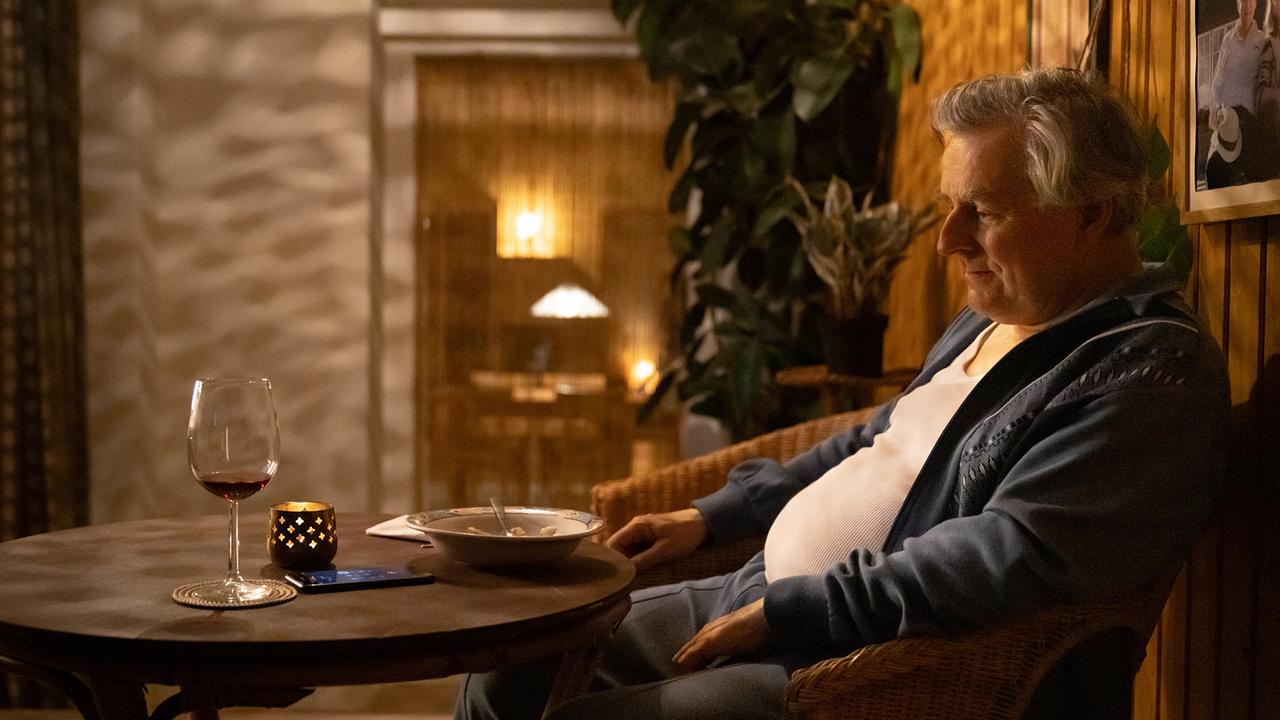 Bertl sitzt abends an einem runden Holztisch bei Kerzenlicht neben einem Glas Rotwein und einem leeren Teller.