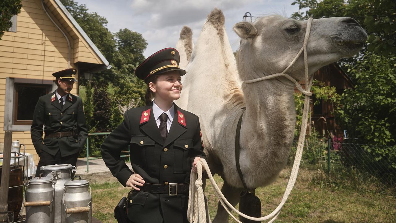 In den 80ern hält Gerti in Polizeiuniform ein weißes Kamel am Strick vor einem Haus, während ihr Kollege Kranzler im Hintergrund steht.