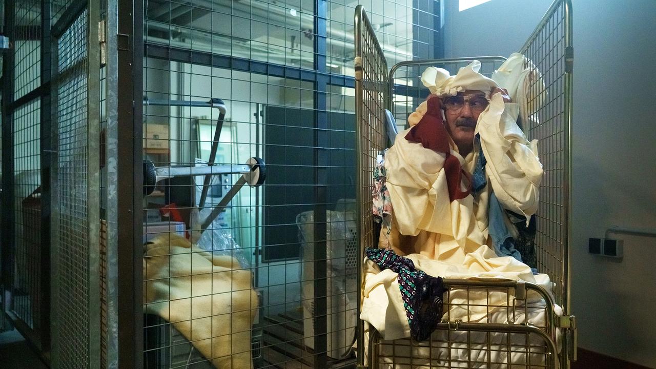 Franco schiebt einen mit Wäsche voll beladenen rollbaren Gittercontainer in einem Lagerraum.