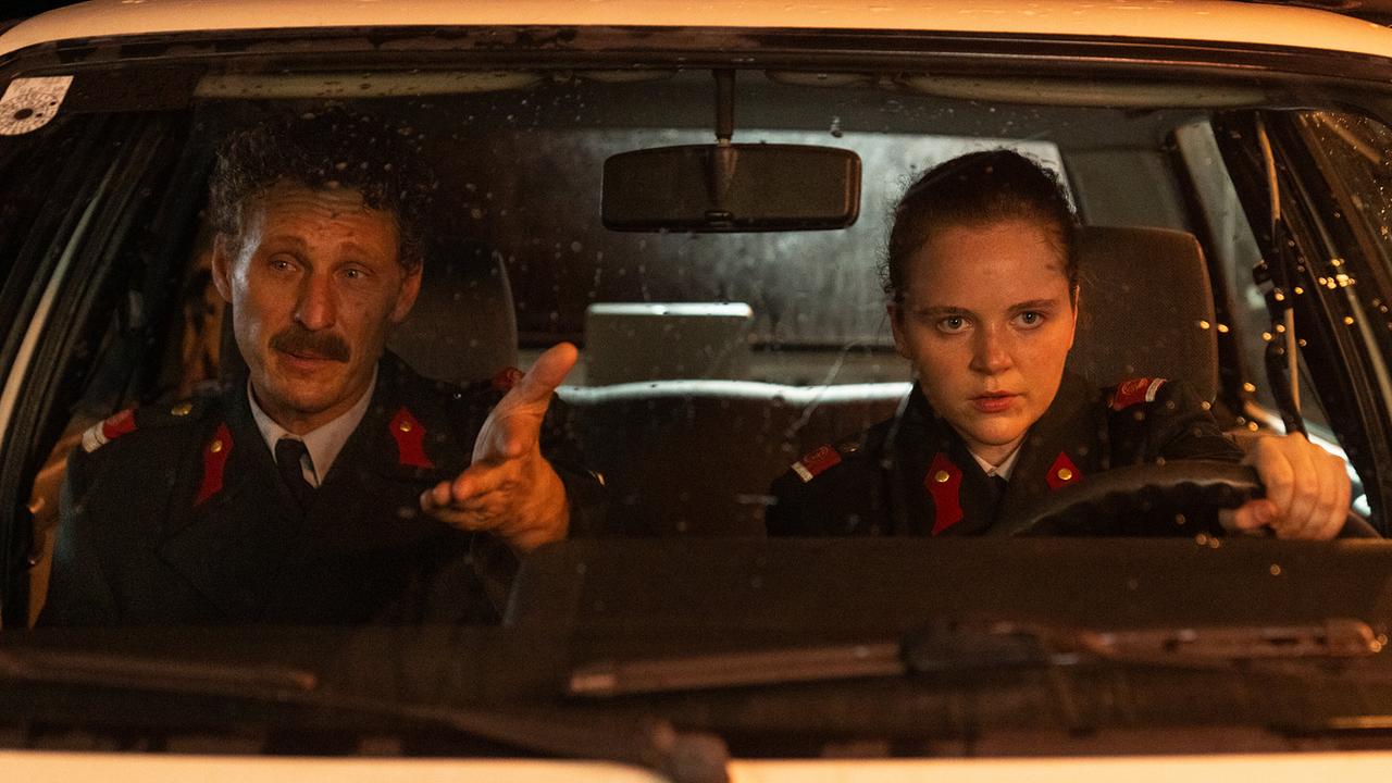 Durch die Windschutzscheibe eines Polizeiautos sind Gerti am Lenkrad und Kranzler am Beifahrersitz, der gestikuliert spricht, zu sehen.