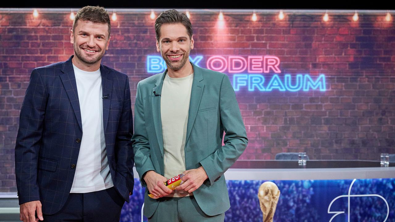 © ORF/Klaus Titzer Thomas Seidl und Philipp Maschl, beide im Anzug, stehen im Studio von der "Fußball Show" vor einer beleuchteten Backsteinwand mit der Aufschrift „Box oder Strafraum“.