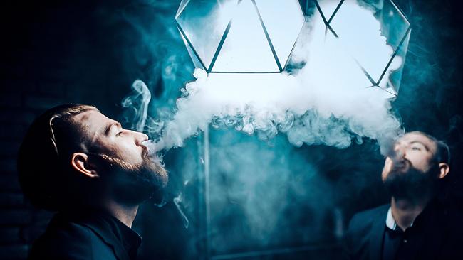 © ORF/RTL/WildBear Entertainment/PBS International/Shutterstock/Anna Berdnik Ein bärtiger Mann steht in einem dunklen Raum vor einem Spiegel und bläst eine dichte, weiße Dampfwolke in den oben montierten Beleuchtungskörper
