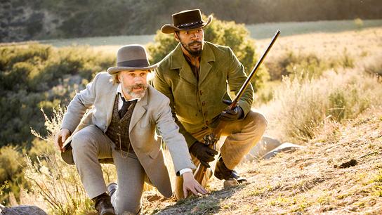 Christoph Waltz als Dr. King Schultz in grauem Anzug und Jamie Foxx als Django in lederner Cowboy-Bekleidung, an einem Hügel duckend beobachten sie etwas, Django hält ein Gewehr in der Hand