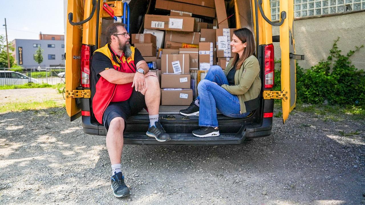 Dok 1: Lisa Gadenstätter sitzt mit einem Lieferanten auf der Ladefläche seines vollbeladenen Lieferautos auf einer seiner Touren.