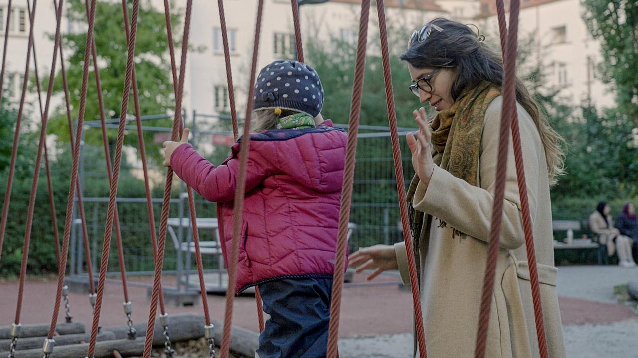Mutter Milena begleitet ihr Kind auf einer Seilbrücke in einem Spielplatz.