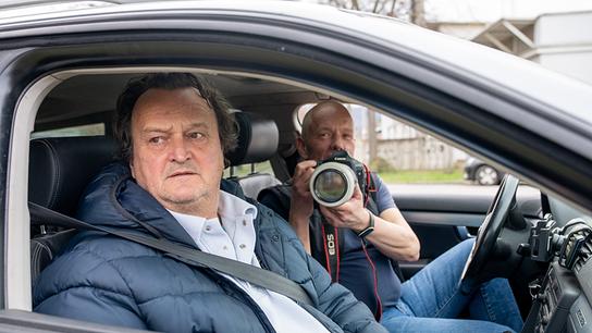 Hanno Settele sitzt mit Berufsdetektiv Markus Schwaiger, der eine Kamera mit Teleobjektiv in den Händen hält, in einem Auto.