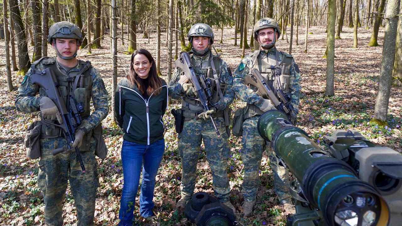 Lisa Gadenstätter steht mit einer Gruppe von Grundwehrdienern während einer Gefechtsübung in einem Wald.