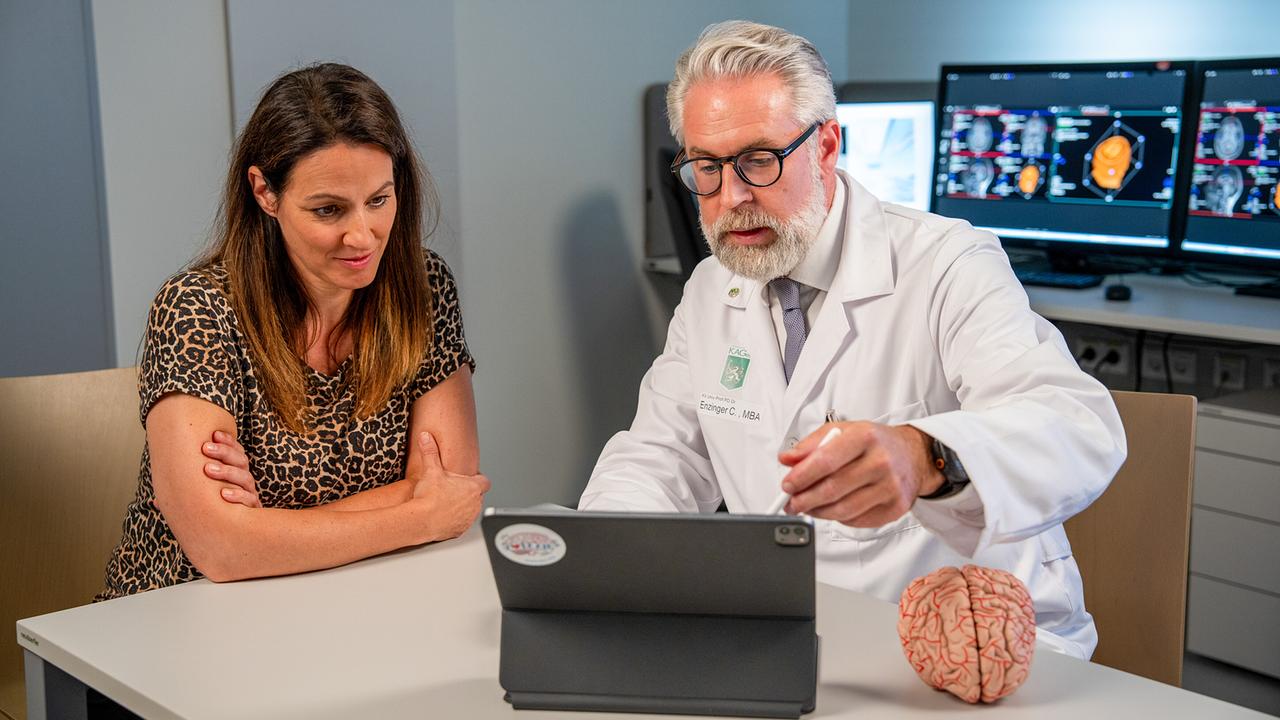 © ORF/Neulandfilm/Stefan Vucsina Neurologe Christian Enzinger erklärt Lisa Gadenstätter anhand eines Tablets und eines Gehirnmodells neurologische Aufnahmen.