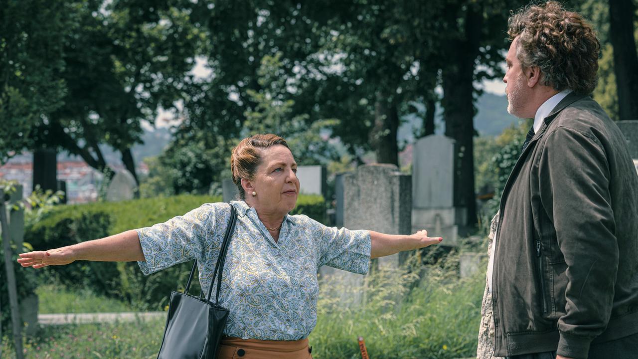 © ORF/Amazon/MGM Auf dem Friedhof hält eine Frau die Arme zur Seite, um einem Mann mit grauer Jacke den Weg zu versperren