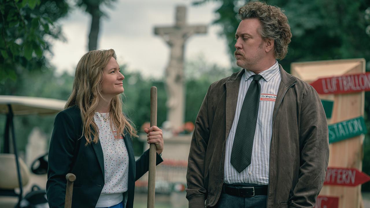 © ORF/Amazon/MGM Eine Frau steht mit zwei Schaufeln am Friedhof neben einem Mann mit brauner Jacke und gestreiftem Hemd, beide sehen sich wertschätzend an