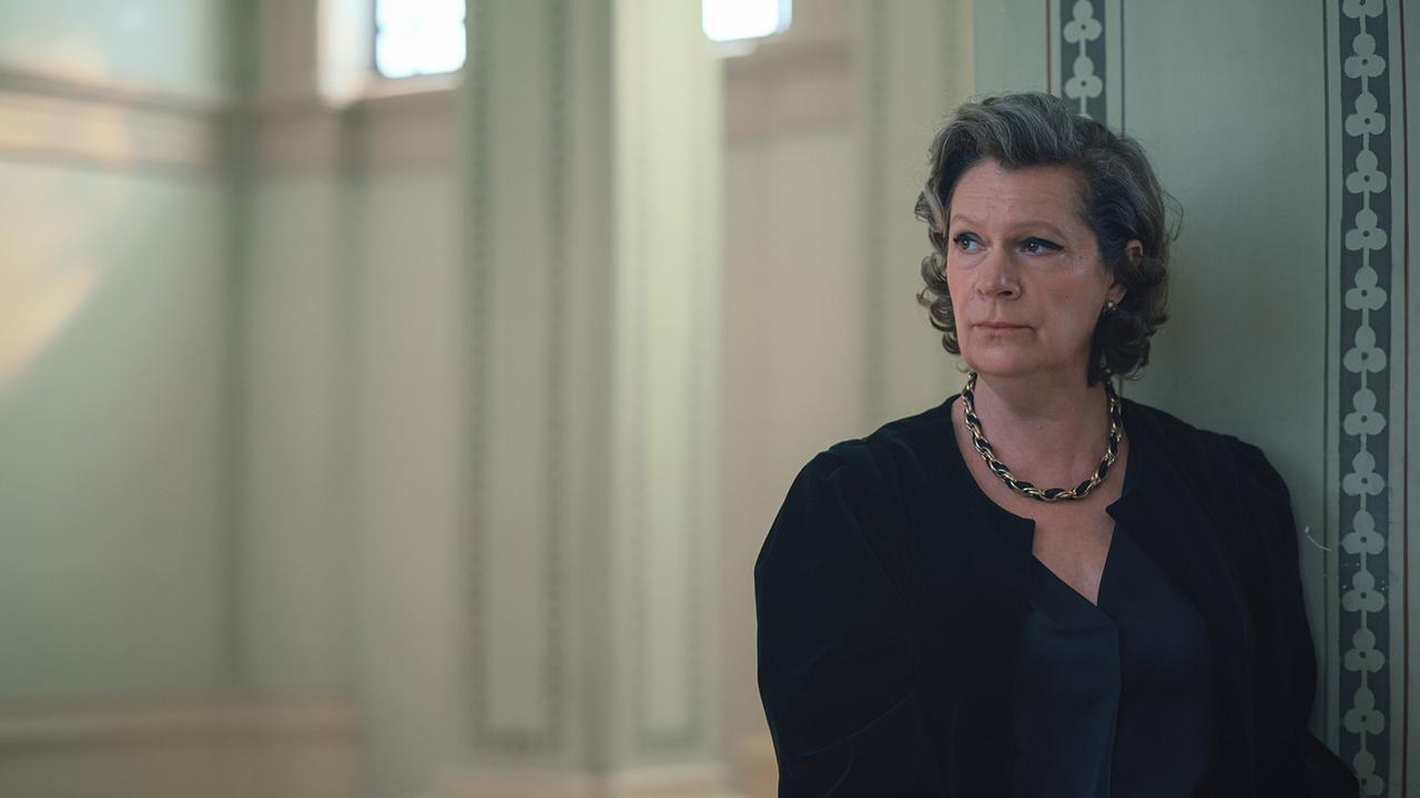 Eine schwarz gekleidete Frau steht in einem historischen Stiegenhaus und blickt nachdenklich zur Seite