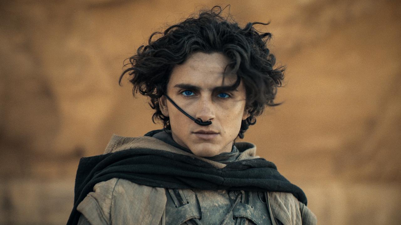 Timothée Chalamet steht als Paul Atreides vor einer beigen Felswand und blickt ernst vor sich hin