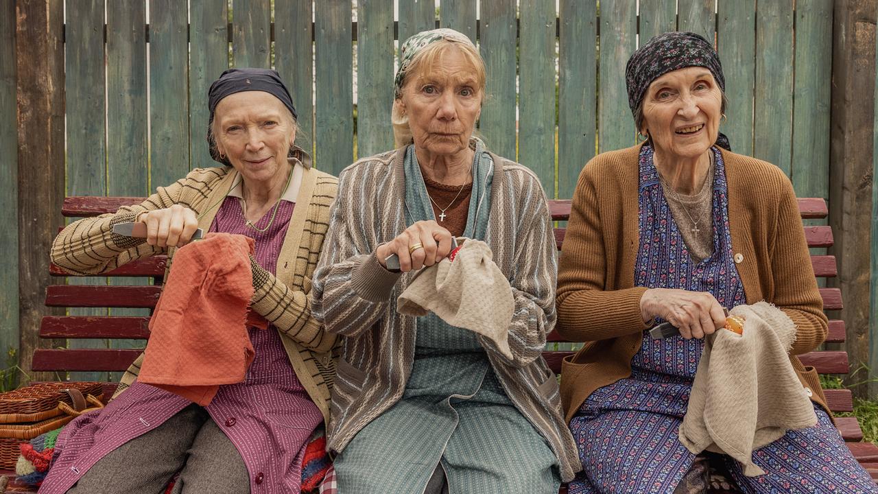 Die drei älteren Frauen Resl Grandits, Baba Sifkovits und Hilda Resetarits sitzen nebeneinander auf einer Bank mit Eierkratzern und Ostereiern in einem Tuch in der Hand.