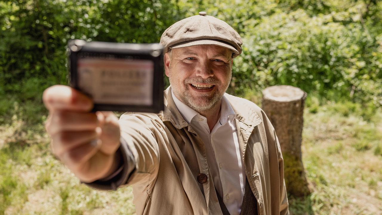 Sifkovits hält auf einem Grundstück in der Natur ein Ausweisdokument direkt in Richtung Kamera.