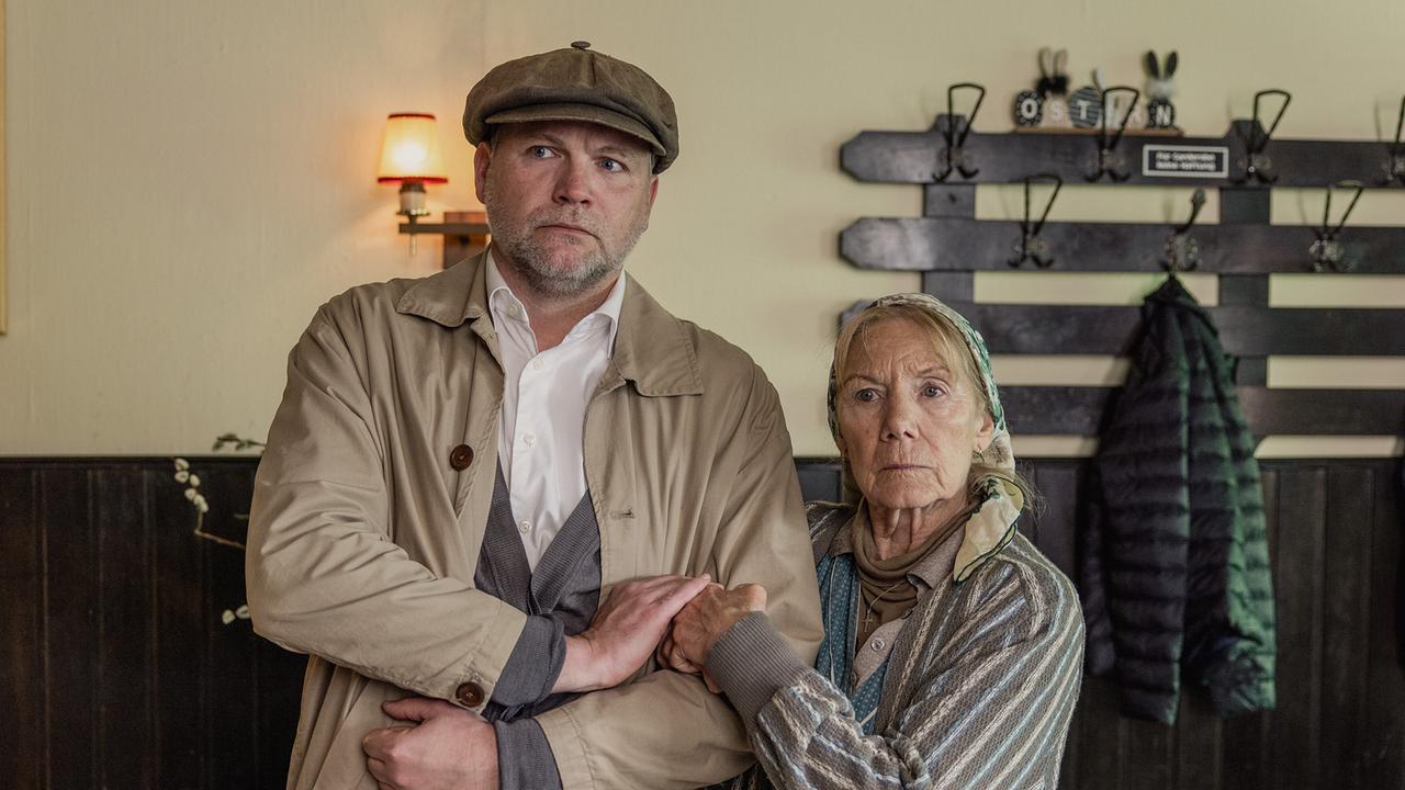 In einem Gastraum steht Sifkovits mit verschränkten Armen, während sich Baba Sifkovits bei ihm einhängt.