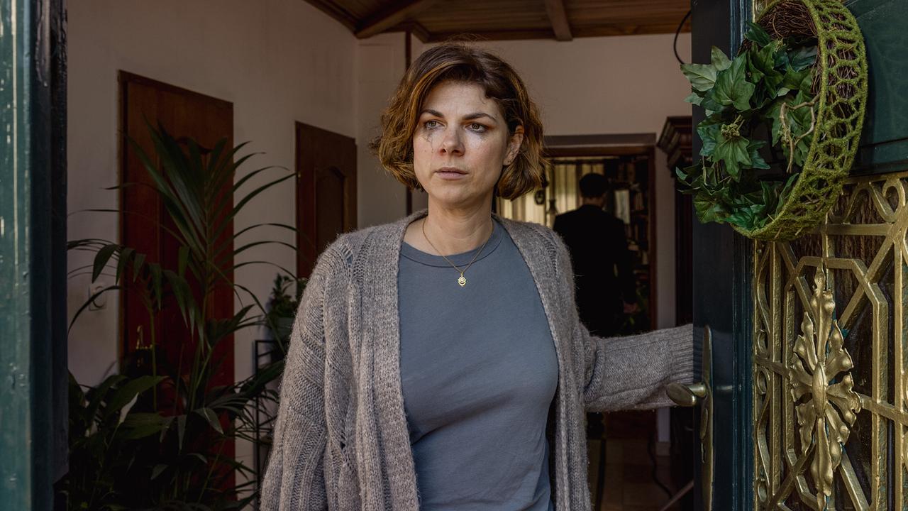 Alexandra Horvatits mit verweinten Augen steht an der offenen Haustür und blickt aus einem gemütlich eingerichteten Eingangsbereich nach draußen.